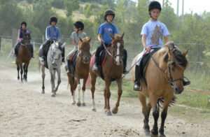 Enfant à cheval lors d’une reprise encadrée dans la carrière de la colonie équitation