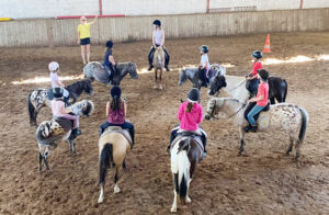 Groupe d’enfants à cheval en cercle dans le manège lors d’une colonie équitation